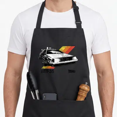 Tablier de cuisine noir avec illustration retro d'une voiture DeLorean et bandes colorées diagonales.