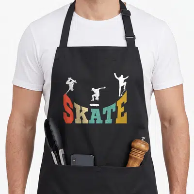 Tablier de cuisine noir avec l'inscription SKATE multicolore et trois silhouettes blanches de skaters effectuant des figures aériennes.