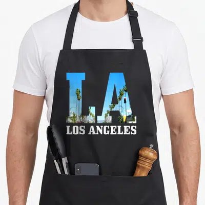 Tablier de cuisine noir avec les lettres LA contenant des palmiers et un feu rouge, LOS ANGELES en blanc en dessous.