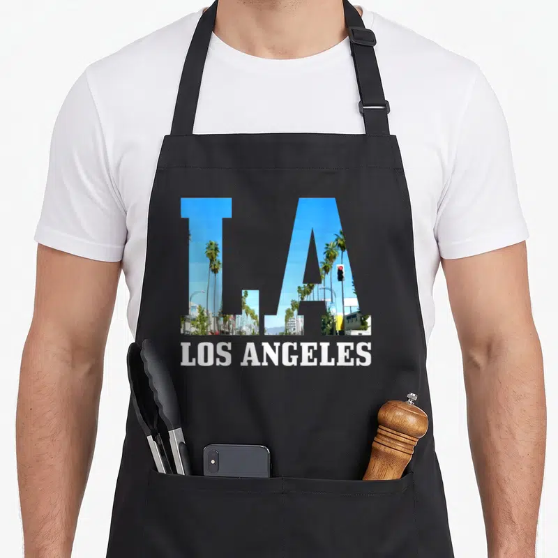 Tablier de cuisine noir avec les lettres LA contenant des palmiers et un feu rouge, LOS ANGELES en blanc en dessous.