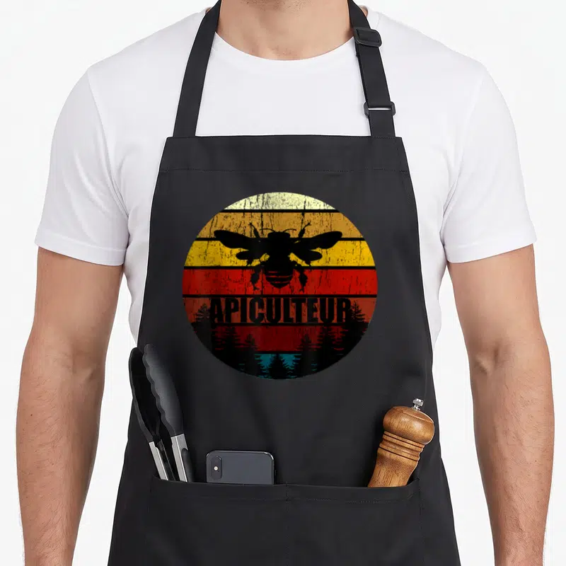 Tablier de cuisine noir avec motif circulaire rétro montrant une abeille et l'inscription apiculteur au-dessus de silhouettes darbres.
