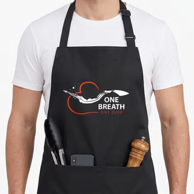 Tablier de cuisine noir avec illustration d'un plongeur en apnée et texte blanc et rouge.