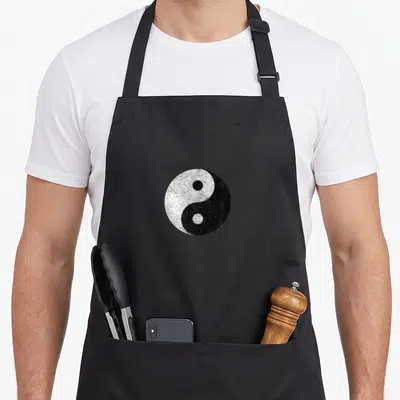 Tablier de cuisine noir avec un grand symbole Yin Yang blanc et noir au style vieilli et texturé.