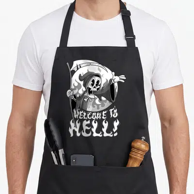 Tablier de cuisine noir avec un squelette cartoon tenant une faux et le texte Bienvenue en hell émergeant de flammes blanches.
