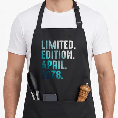 Tablier de cuisine noir avec inscription Limited Edition Avril 1978 en lettres dégradées bleu turquoise et blanches.