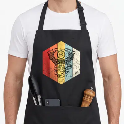 Tablier de cuisine noir avec illustration hexagonale d'un moteur vintage multicolore sur fond texturé.