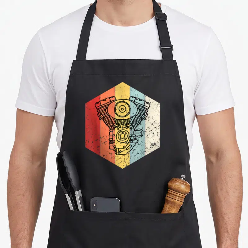 Tablier de cuisine noir avec illustration hexagonale d'un moteur vintage multicolore sur fond texturé.