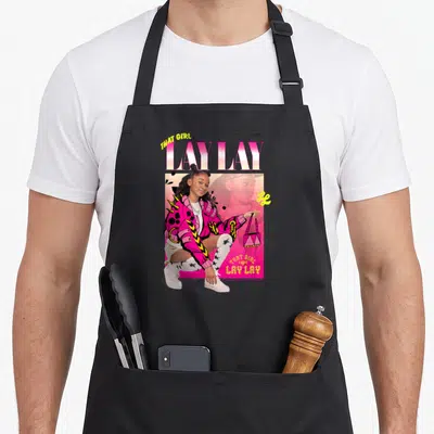 Tablier de cuisine noir avec illustration colorée d'une jeune femme en veste rose et texte That Girl Lay Lay.
