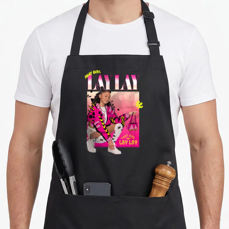 Tablier de cuisine noir avec illustration colorée d'une jeune femme en veste rose et texte That Girl Lay Lay.