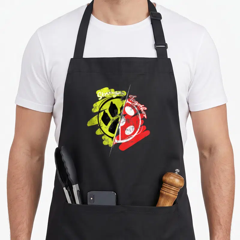 Tablier de cuisine noir avec un logo circulaire jaune et rouge divisé par une ligne blanche et du texte manuscrit.
