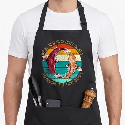 Tablier de cuisine noir avec deux poissons koi rouge et orange sous un soleil couchant retro.