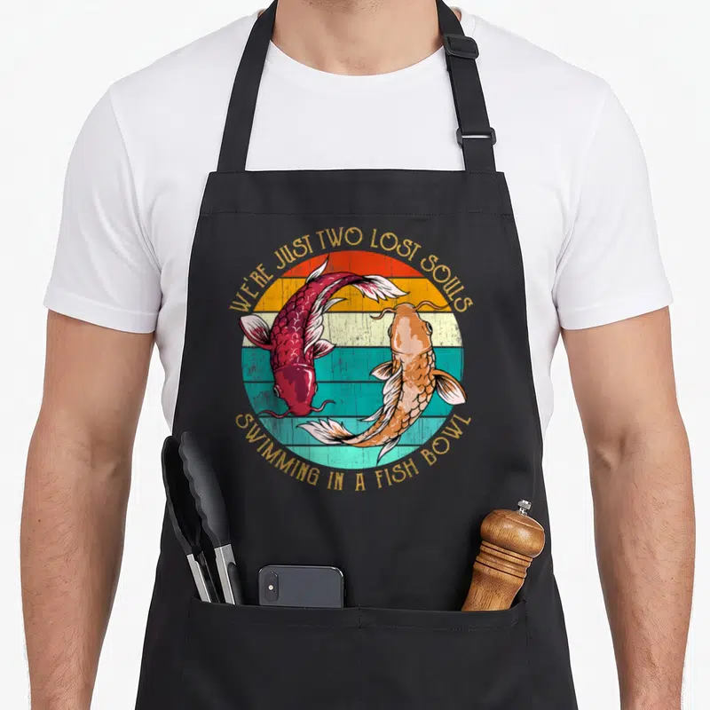 Tablier de cuisine noir avec deux poissons koi rouge et orange sous un soleil couchant retro.