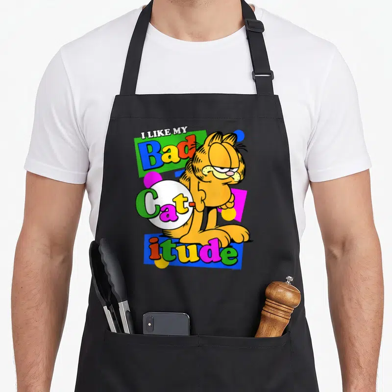 Tablier de cuisine noir avec l'illustration colorée de Garfield et le texte I Like My Bad Catitude en style rétro.