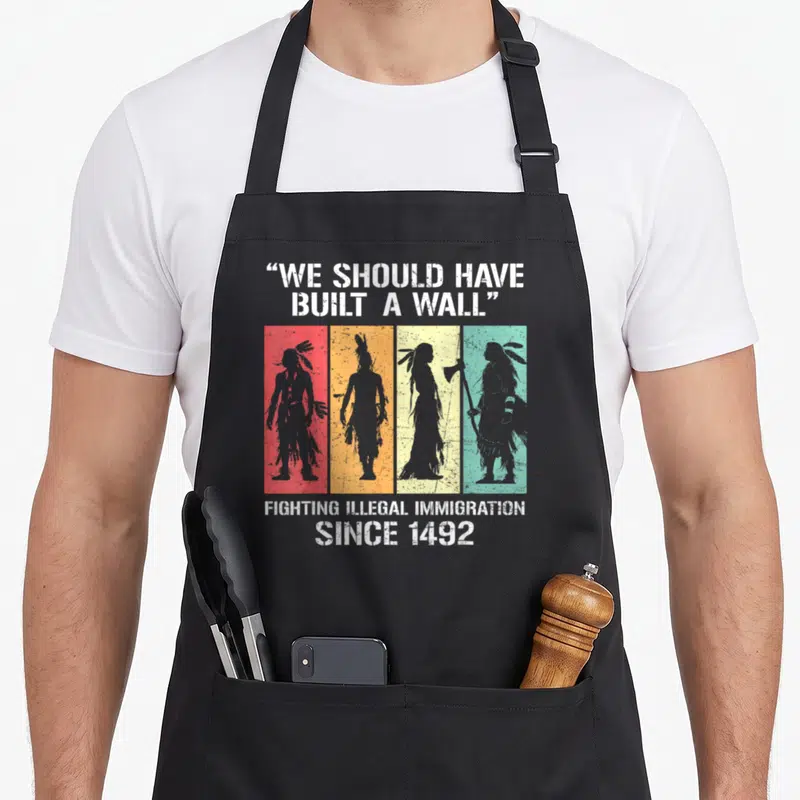 Tablier de cuisine noir avec silhouettes amérindiennes colorées et texte satirique en anglais.