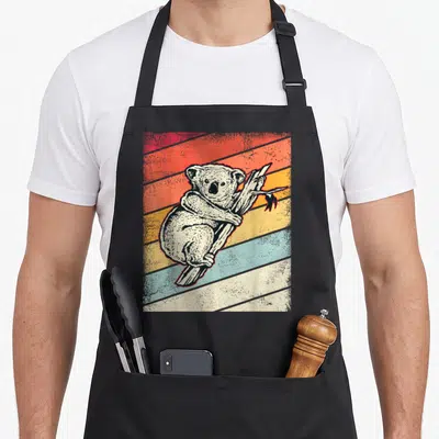 Tablier de cuisine noir avec illustration d'un koala accroché à une branche sur fond de bandes diagonales colorées style rétro.