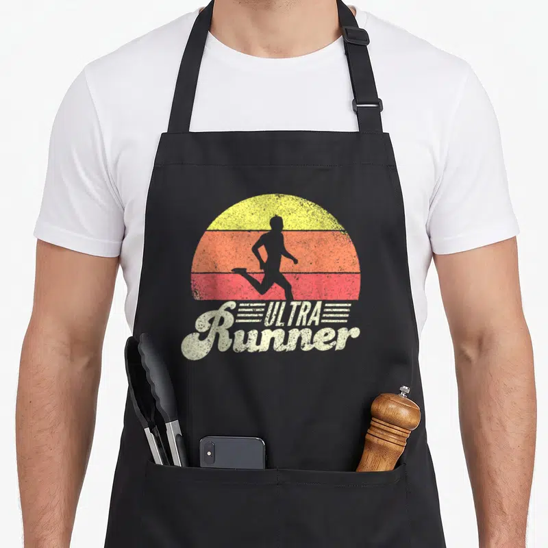 Tablier de cuisine noir avec silhouette de course et texte Ultra Runner Classic sur fond de soleil rétro.