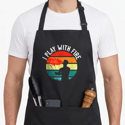 Tablier de cuisine noir avec silhouette crachant des flammes sur fond de soleil arc-en-ciel vintage
