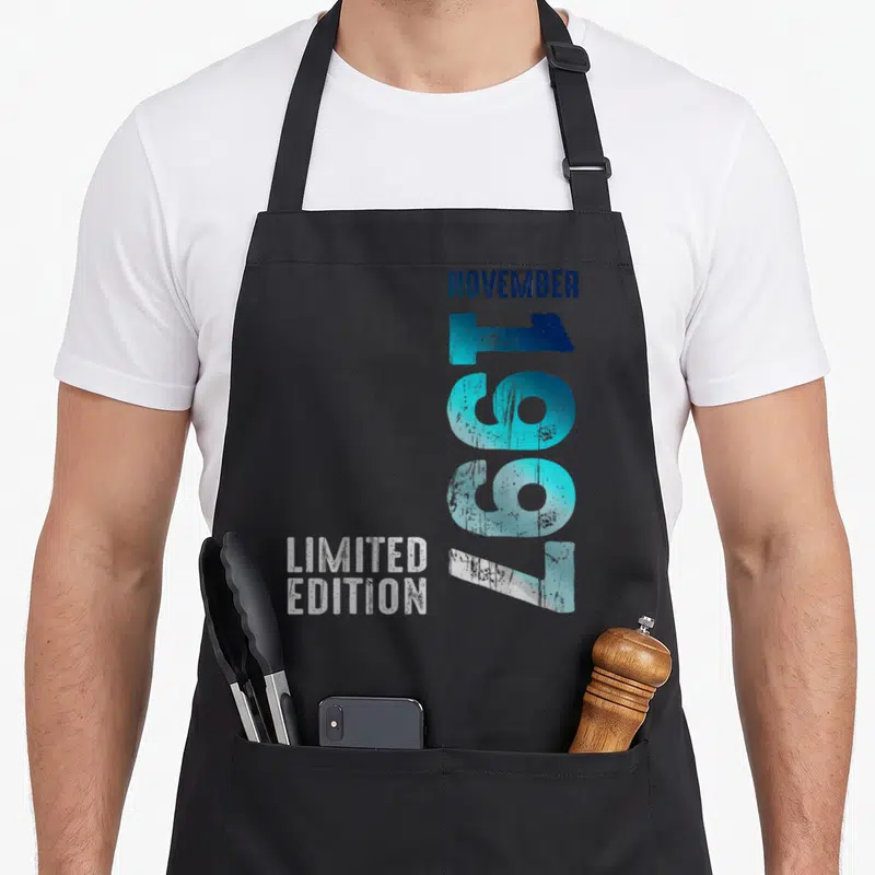 Tablier de cuisine noir avec l inscription Novembre 1997 et Limited Edition en typographie rétro bleue et blanche.