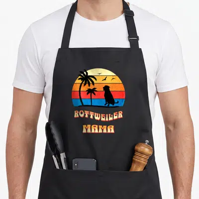 Tablier de cuisine noir avec illustration rétro Rottweiler Mama et palmiers sur fond de sunset coloré.