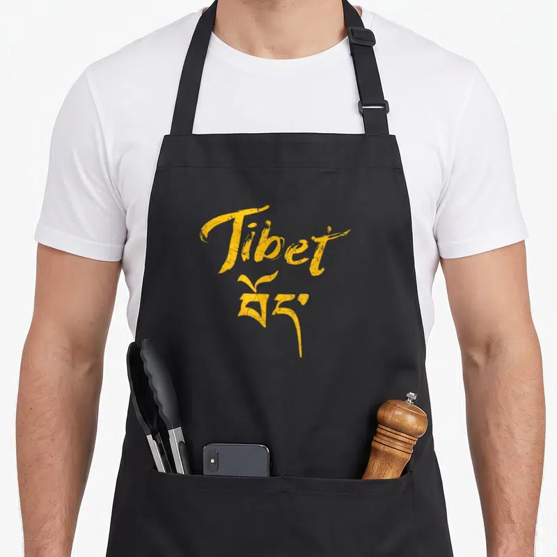 Tablier de cuisine noir avec l'inscription Tibet en jaune et des caractères asiatiques stylisés.