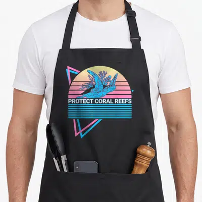 Tablier de cuisine noir avec illustration rétro d'une tortue et du texte Protect Coral Reefs sur fond de soleil couchant.