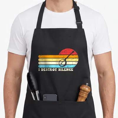 Tablier de cuisine noir avec illustration de banjo sur fond de rayures colorées et texte I Destroy Silence en bas.