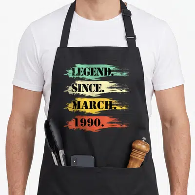 Tablier de cuisine noir avec les mots Legend Since March 1990 sur fond de touches colorées dégradées.