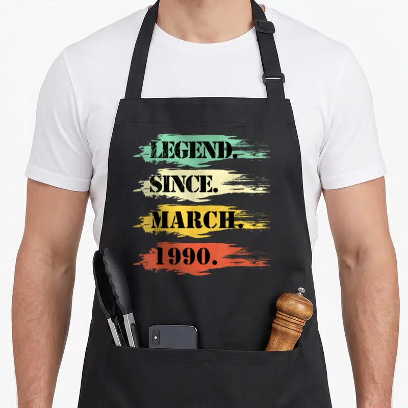 Tablier de cuisine noir avec les mots Legend Since March 1990 sur fond de touches colorées dégradées.