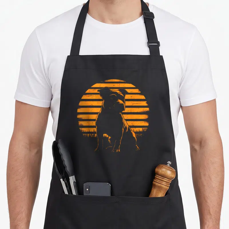 Tablier de cuisine noir avec silhouette orange d'un Staffordshire Bull Terrier devant un soleil rayé style rétro.