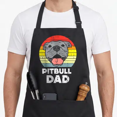 Tablier de cuisine noir avec illustration d'un Pitbull Dad sur fond de soleil couchant aux couleurs dégradées.