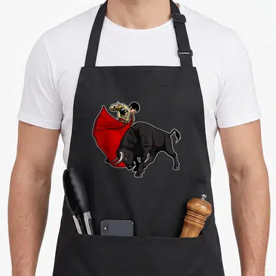 Tablier de cuisine noir avec illustration d'un matador en costume doré brandissant une cape rouge devant un taureau noir aux cornes acérées.