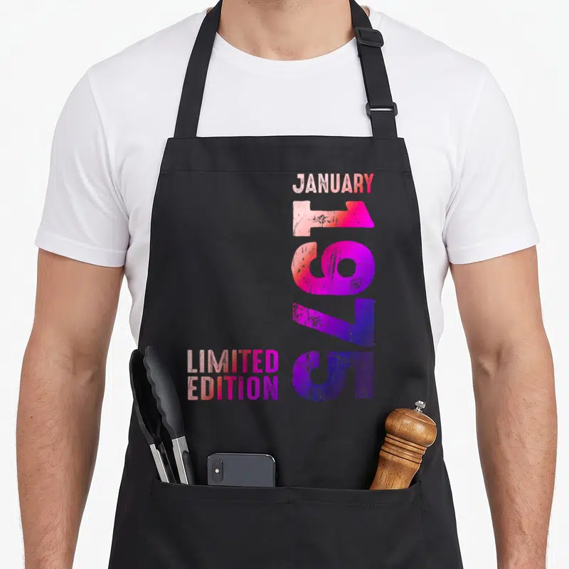 Tablier de cuisine noir avec typographie verticale colorée indiquant janvier 1975 et limited edition en dégradé rose et violet.