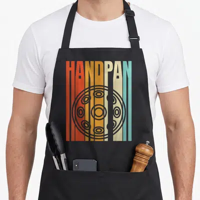 Tablier de cuisine noir avec illustration retro d'un handpan et le mot HANDPAN en lettres colorées verticales.