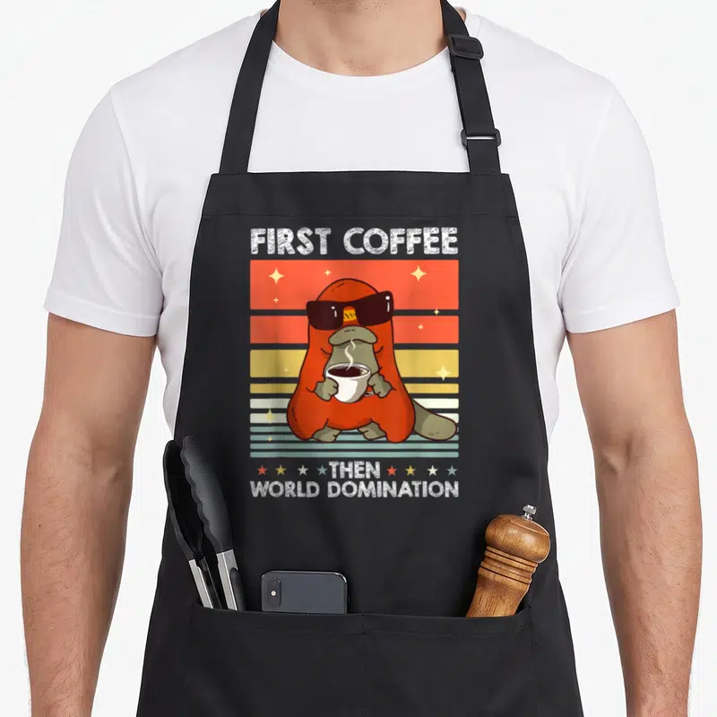 Tablier de cuisine noir avec illustration rétro d'un ornithorynque en lunettes de soleil tenant une tasse de café sur fond coloré.