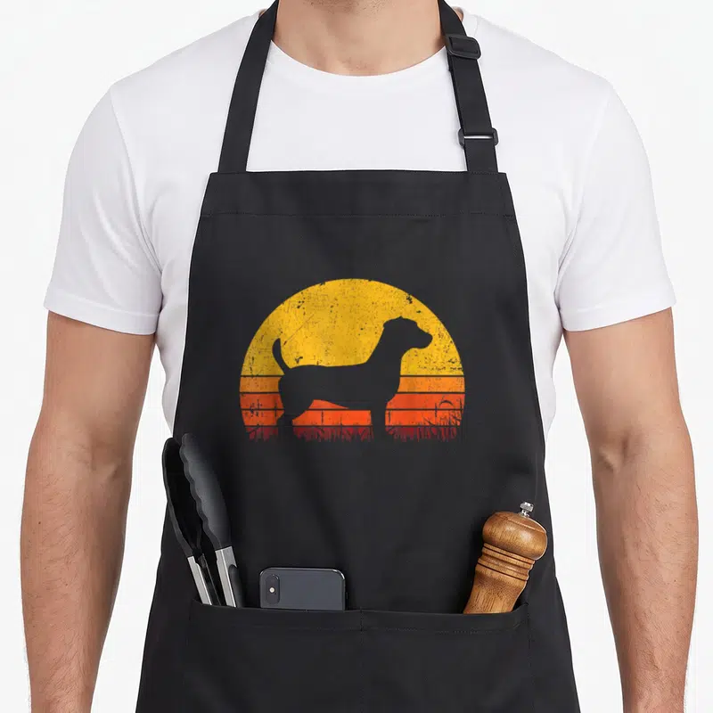 Tablier de cuisine noir avec silhouette Jack Russell Terrier sur fond de soleil couchant orange et jaune style rétro.