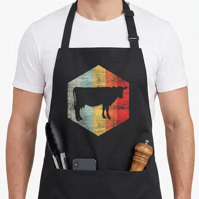 Tablier de cuisine noir avec silhouette de vache sur fond hexagonal multicolore à l'aspect vieilli