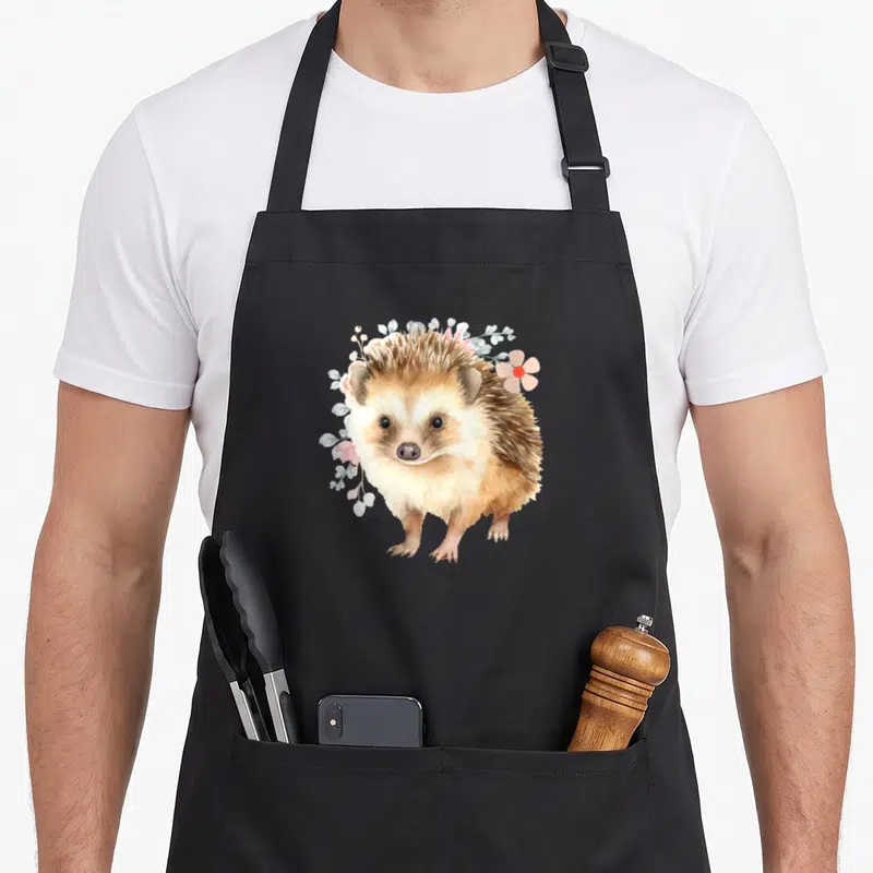 Tablier de cuisine noir avec illustration d'un hérisson retro art entouré de fleurs roses et de feuilles bleutées.