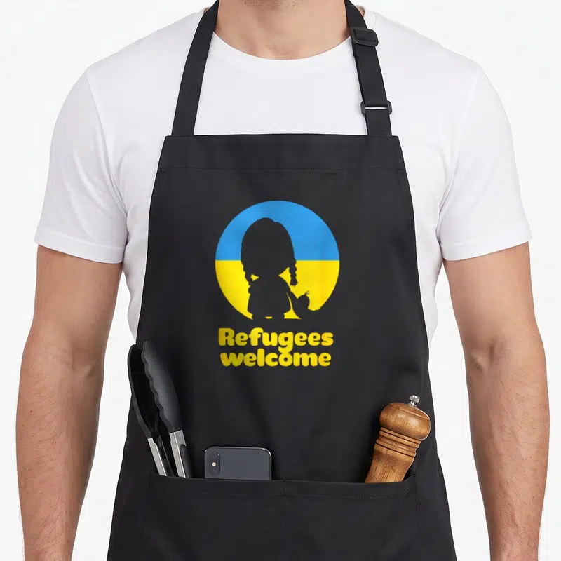 Tablier de cuisine noir avec une silhouette d'enfant sur un cercle bleu et jaune portant l'inscription Refugees welcome en jaune.