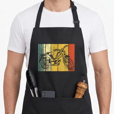 Tablier de cuisine noir avec illustration rétro d'une mobylette sur fond de bandes vertes, jaunes et rouges texturées.