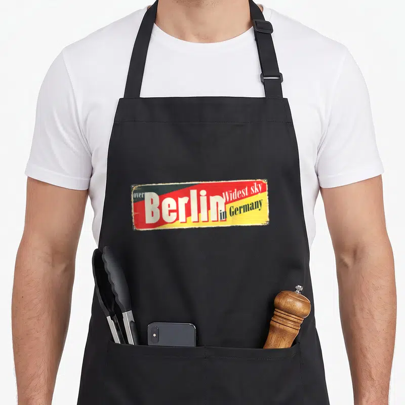 Tablier de cuisine noir avec une illustration rectangulaire imitant une enseigne vintage aux couleurs rouge, jaune et noire.
