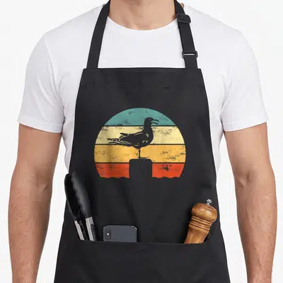 Tablier de cuisine noir avec illustration d'une mouette sur un soleil rayé retro aux teintes pastel.