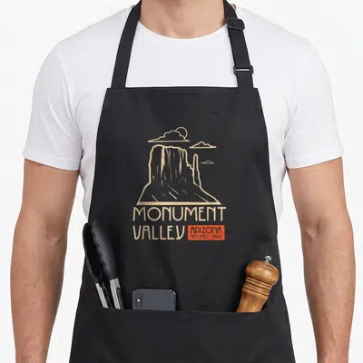 Tablier de cuisine noir avec illustration rétro du Monument Valley et texte beige et orange.