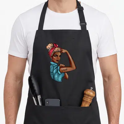 Tablier de cuisine noir avec illustration d'une femme aux cheveux blonds coiffés en chignon et un bandana rouge, arborant le mot Vaxed.