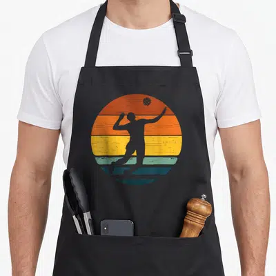 Tablier de cuisine noir avec illustration rétro d'un joueur de volley-ball sur fond de soleil coloré