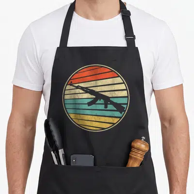 Tablier de cuisine noir avec illustration circulaire d'un fusil AK-47 sur fond rayé multicolore retro.