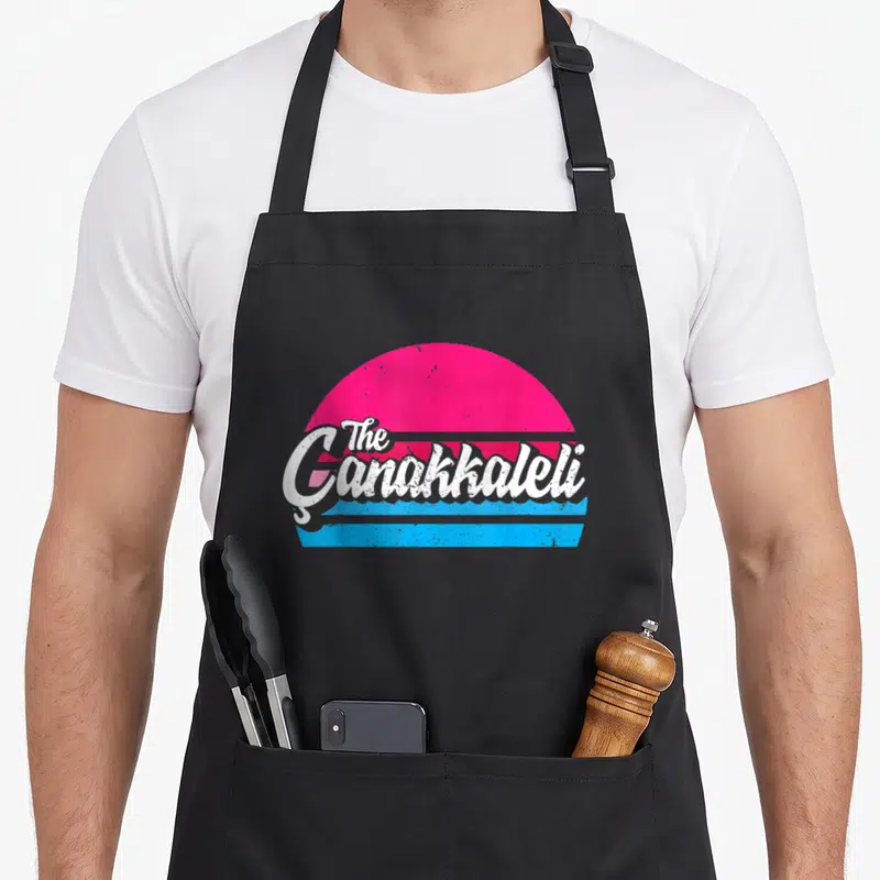 Tablier de cuisine noir avec le logo The Çanakkaleli sur fond de soleil rose et bandes bleues style rétro.