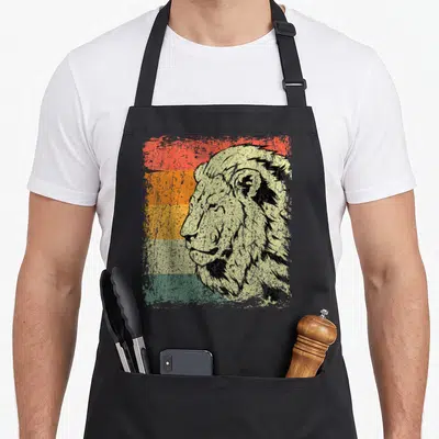Tablier de cuisine noir avec tête de lion de profil sur fond de bandes colorées délavées rouge orange jaune vert et beige.