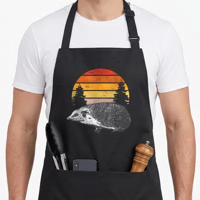 Tablier de cuisine noir avec illustration hérisson style gravure devant soleil couchant bandes orange et jaunes vintage