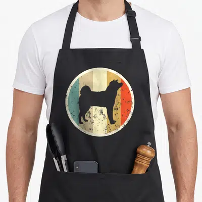 Tablier de cuisine noir avec un motif circulaire représentant un Akita Inu sur fond de bandes verticales colorées et texturées.
