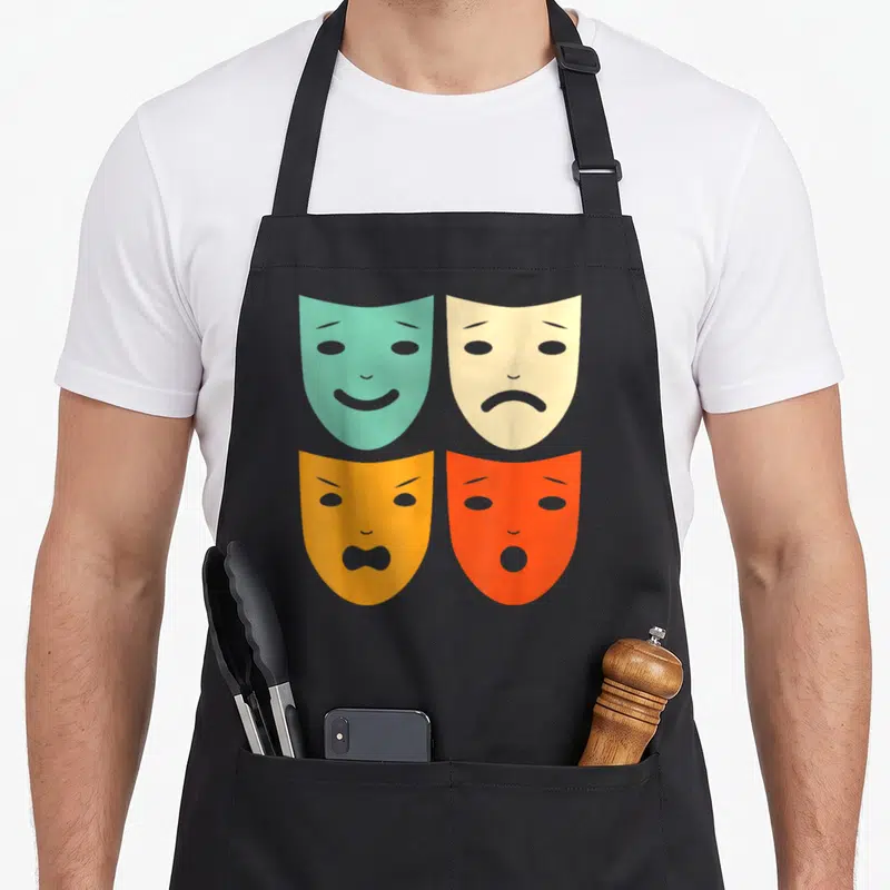 Tablier de cuisine noir avec quatre masques de théâtre vintage aux expressions variées et couleurs pastel.